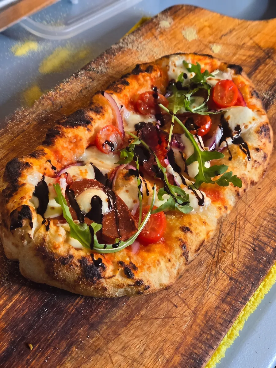 Fresh La Ricetta pizza with cherry tomatoes, arugula and balsamic glaze on its wooden board